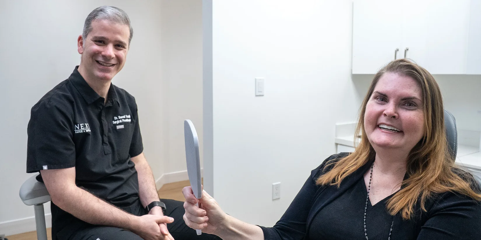 Patient looking into a mirror at her new smile at Next Smile+Implant